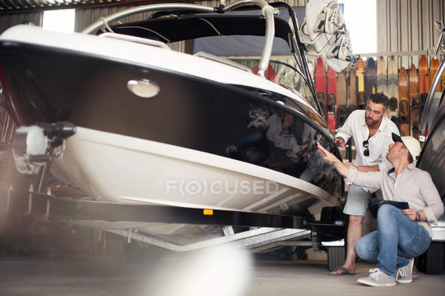 Deux hommes vérifient la carrosserie du bateau à moteur en atelier de réparation — Photo de stock