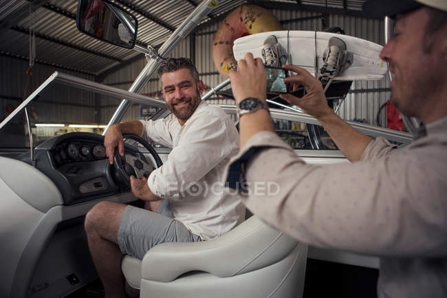 Homem fotografando colega em barco na oficina de reparação — Fotografia de Stock
