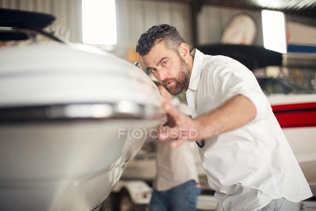 Homme vérifiant carrosserie sur bateau en atelier de réparation — Photo de stock