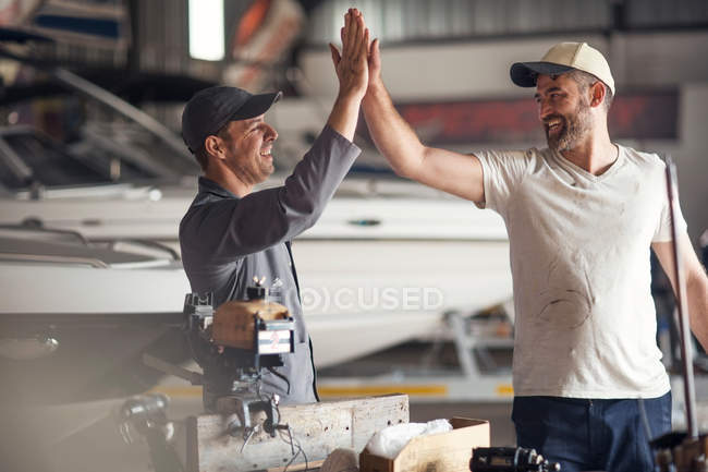 Two men high fiving in boat repair workshop — Stock Photo