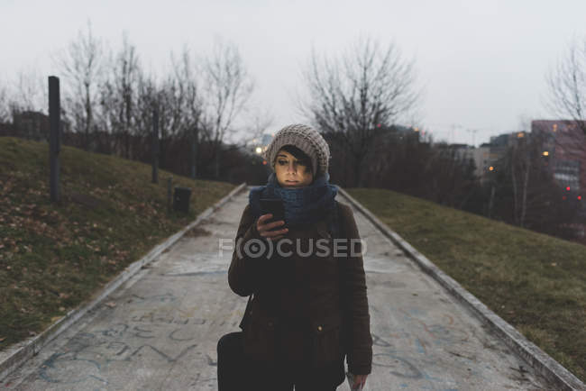 Mochileiro andando no parque e olhando para o smartphone — Fotografia de Stock