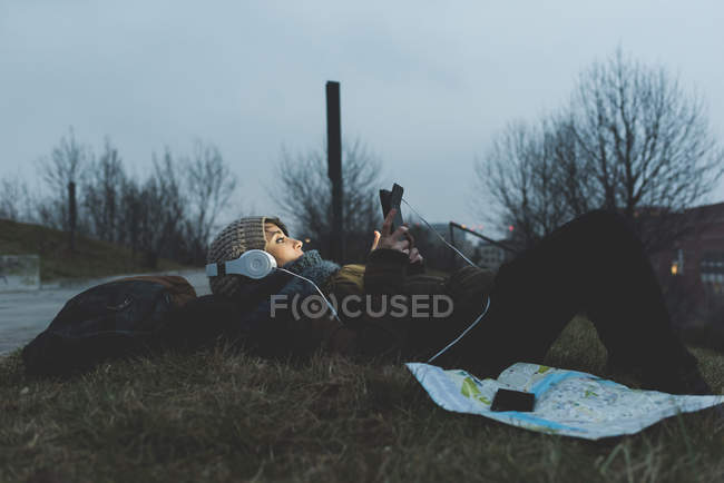 Backpacker lying in park and looking at smartphone — Stock Photo
