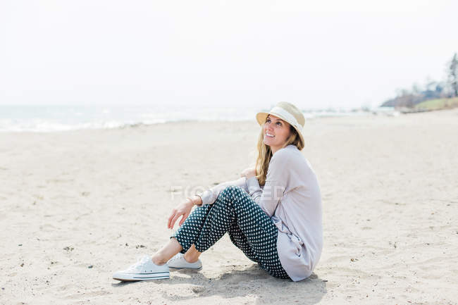 Mulher de chapéu de sol sentado na praia — Fotografia de Stock