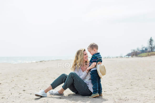 Mujer sentada en la playa y jugando con su hijo - foto de stock