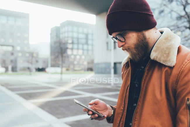 Hipster en la ciudad mirando el teléfono inteligente - foto de stock