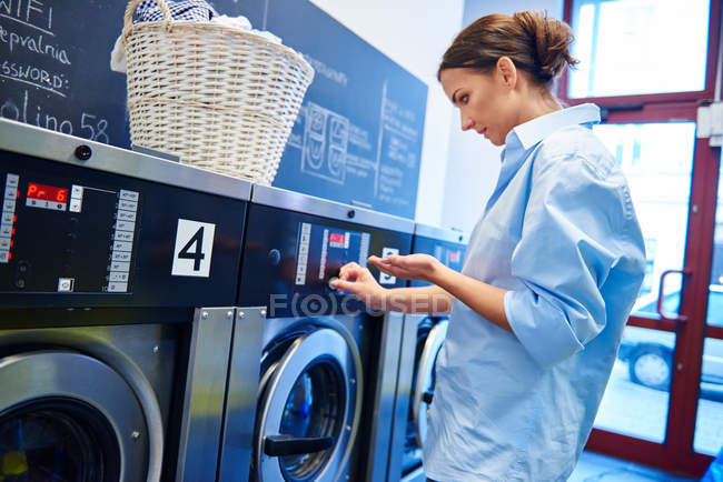 Mulher inserindo moedas na máquina de lavar roupa — Fotografia de Stock