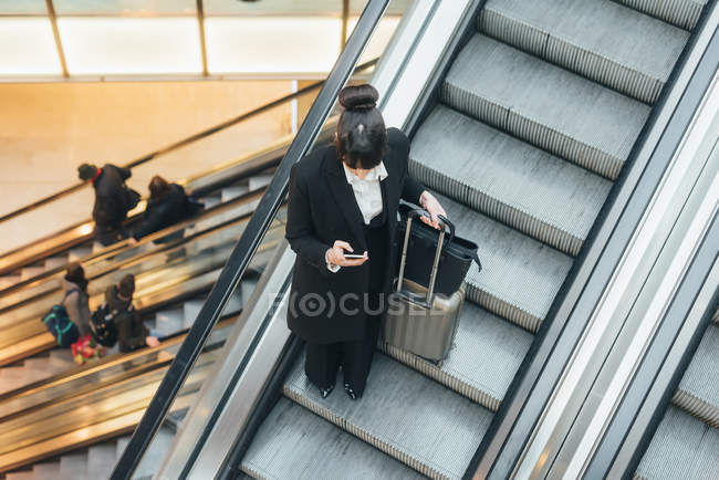 Businesswoman using mobile phone on escalator — Stock Photo