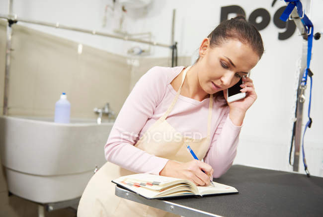 Woman on smartphone writing in diary — Stock Photo