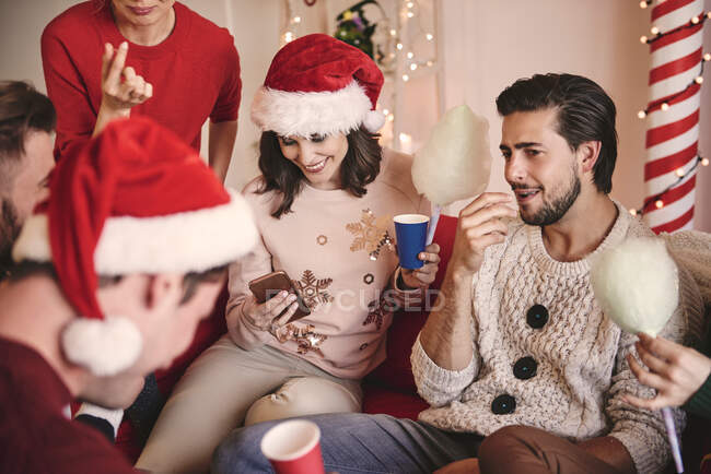 Jovens mulheres e homens olhando para smartphone no sofá na festa de Natal — Fotografia de Stock