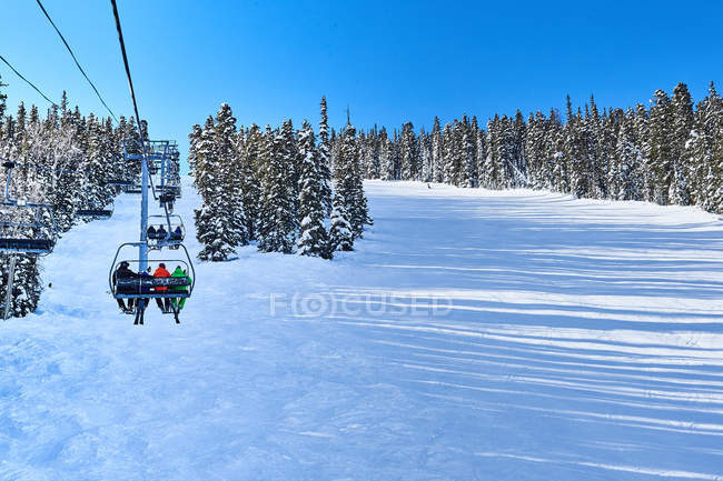 Skiers on ski lift moving up snow covered landscape — Stock Photo