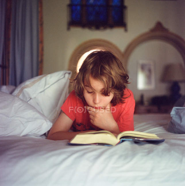 Boy relaxing on bed, reading book — Stock Photo