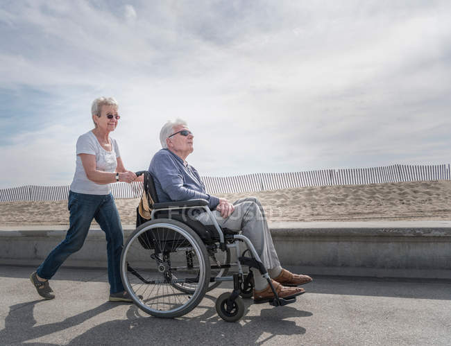 Женщина толкает мужа в инвалидной коляске — стоковое фото