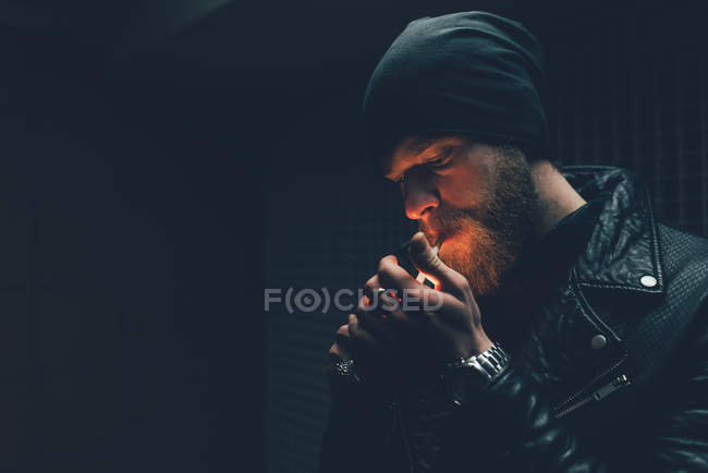 Hipster en bonnet tricoté allumant cigarette — Photo de stock