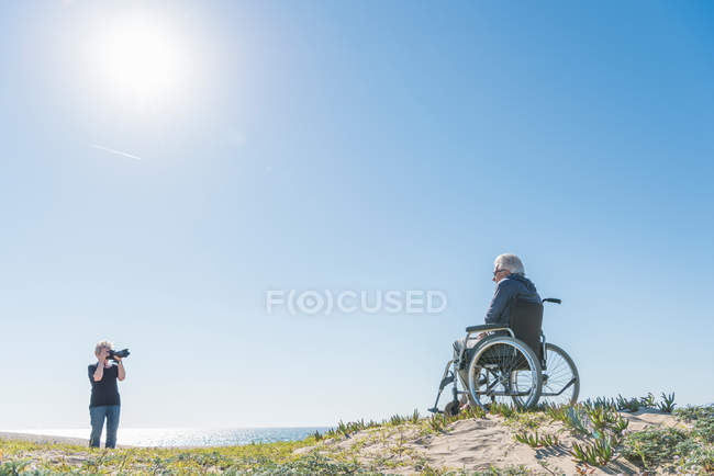 Женщина фотографирует мужа в инвалидном кресле — стоковое фото