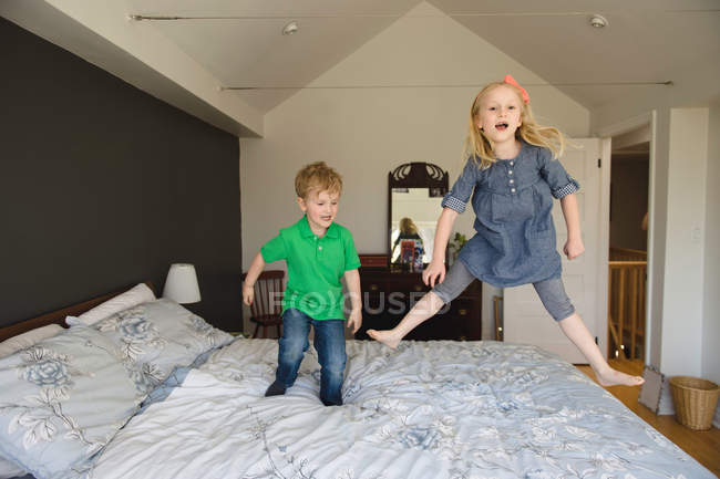 Chica y hermano saltando en la cama - foto de stock