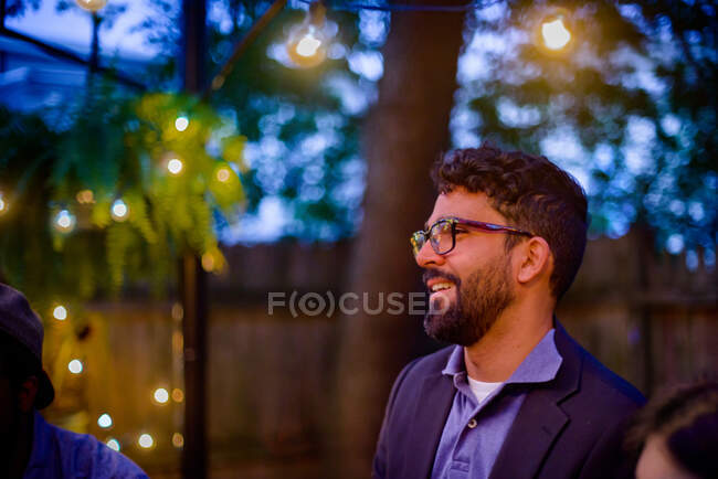 Чоловік середнього віку на вечірці в саду, в сутінках, посміхаючись — стокове фото