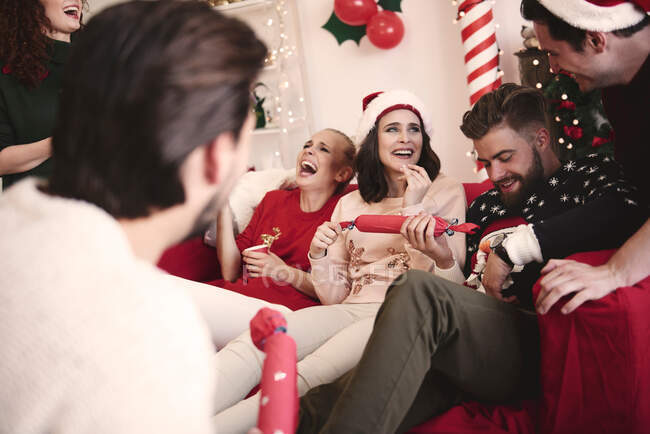 Junge erwachsene Freunde ziehen Weihnachtscracker auf Sofa bei Weihnachtsfeier — Stockfoto