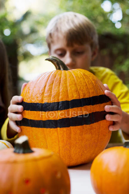 Boy lifting large stripe painted pumpkin — Stock Photo
