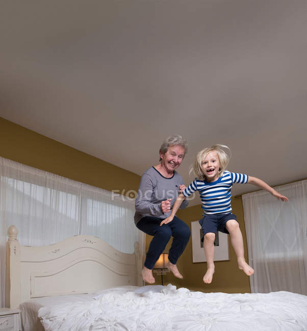 Enkel und Großmutter springen auf Bett — Stockfoto