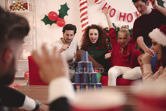 Junge erwachsene Freunde werfen bei Weihnachtsfeier Ball auf Pappbecherpyramide — Stockfoto