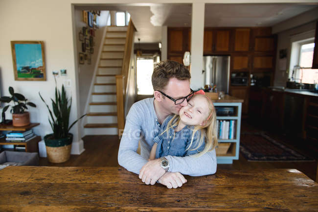 Man sitting at kitchen kissing daughter — Stock Photo