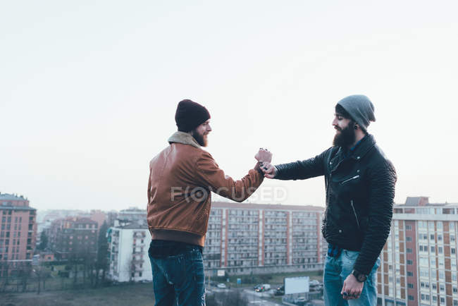 Male hipsters fist bumping above cityscape — Stock Photo