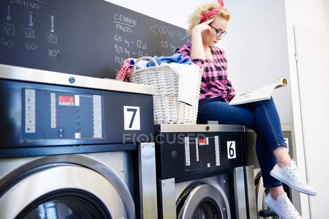 Mulher leitura revista na lavanderia — Fotografia de Stock