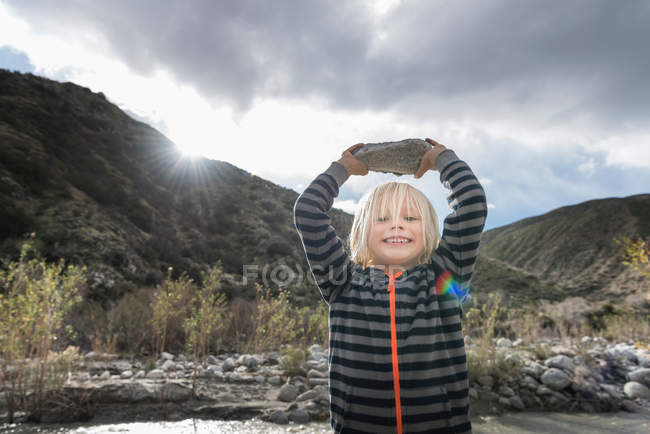 Cute boy holding up rock — Stock Photo