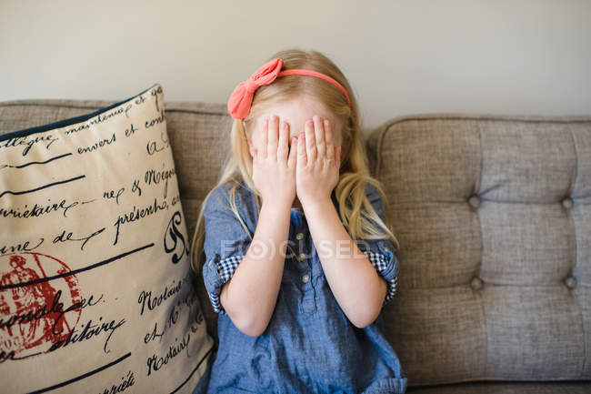 Menina no sofá cobrindo seu rosto — Fotografia de Stock