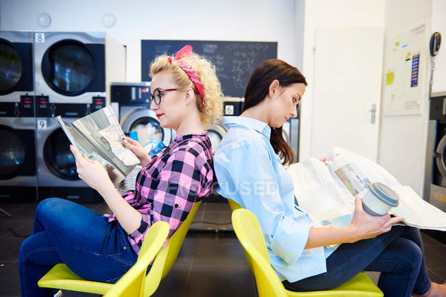 Women reading newspapers in laundrette — Stock Photo