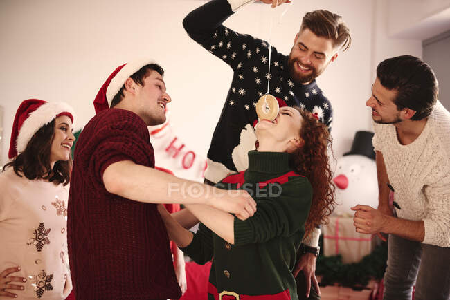 Young woman eating dangled doughnut at christmas party — Stock Photo