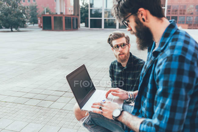Hipster sitzen an der Wand und tippen auf Laptop — Stockfoto
