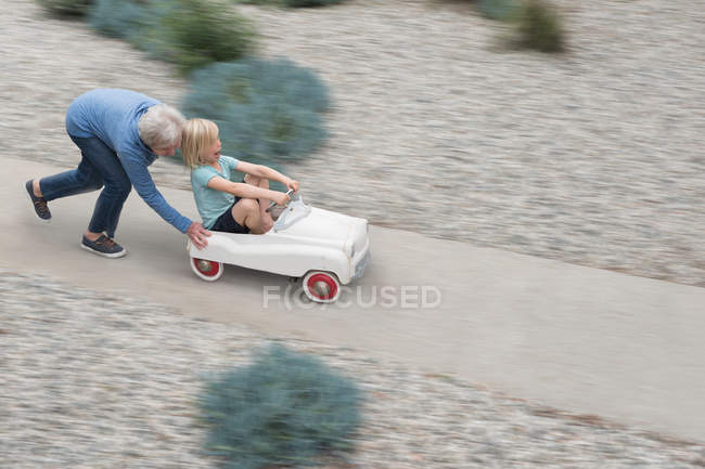 Grandmother pushing grandson on toy car — Stock Photo