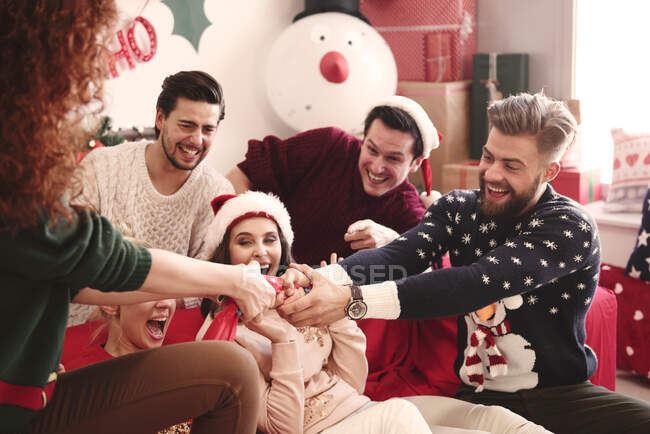 Jovens amigos adultos puxando biscoitos de Natal no sofá na festa de Natal — Fotografia de Stock