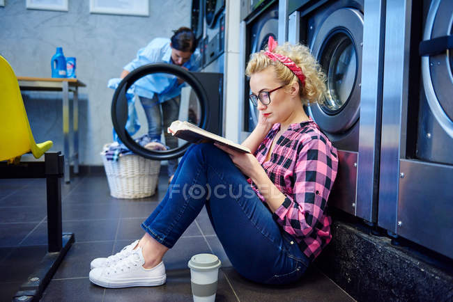 Mujer sentada en el piso de la lavandería - foto de stock