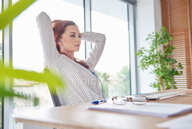 Woman at desk hands behind head — Stock Photo