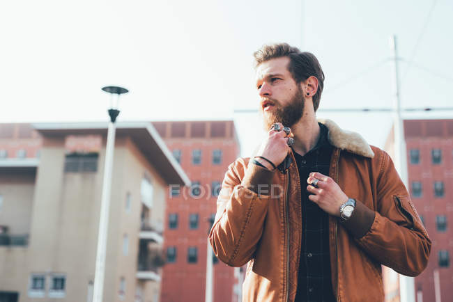 Hipster stroking beard on housing estate — Stock Photo