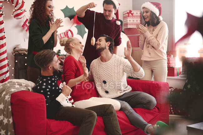 Young man eating dangled doughnut at christmas party — Stock Photo