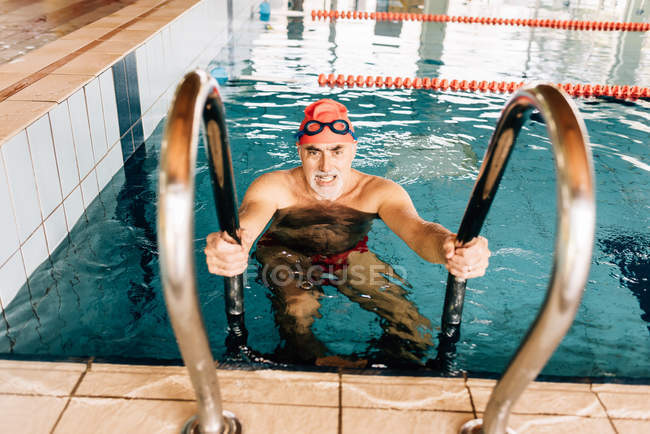 Hombre usando escalera en piscina - foto de stock