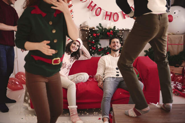 Amigos viendo a un joven bailando en la mesa en la fiesta de Navidad - foto de stock