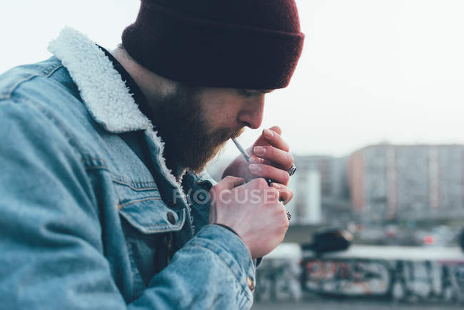 Хипстер в вязаной шляпе, зажигающий сигарету — стоковое фото