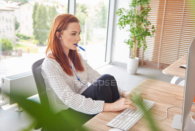 Woman at desk wearing earbuds — Stock Photo