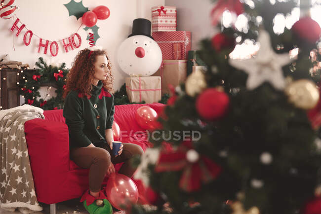 Triste jeune femme assise seule sur le canapé à Noël — Photo de stock