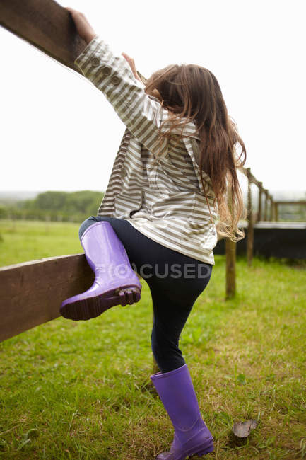Девушка лезет на деревянный забор на открытом воздухе — стоковое фото