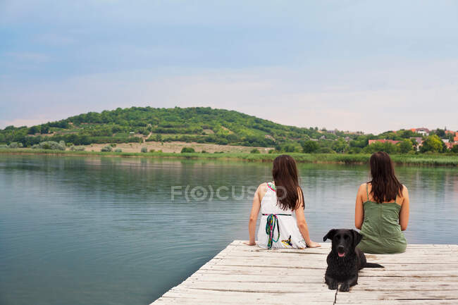 Женщины сидят с собакой на пирсе — стоковое фото