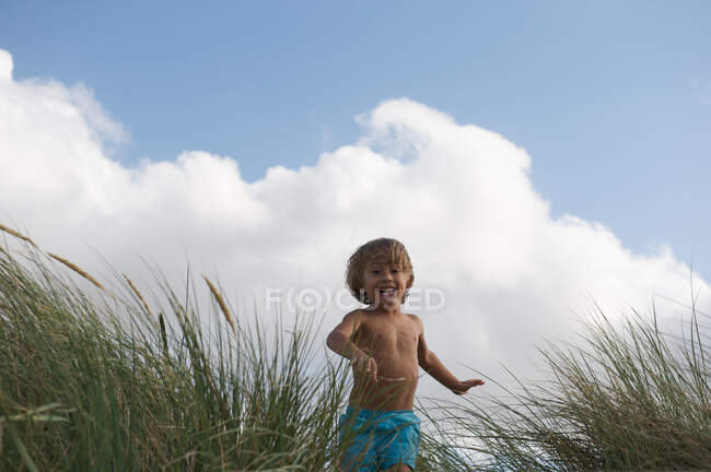 Niño corriendo en duna de arena cubierta de hierba - foto de stock