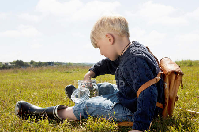 Мальчик наполняя банку в травянистом поле — стоковое фото