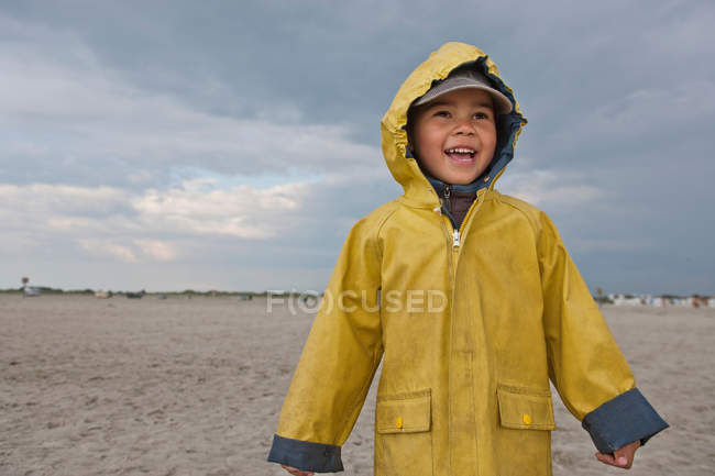 Menino sorrindo vestindo capa de chuva na praia — Fotografia de Stock