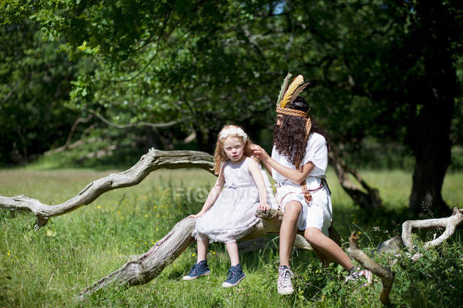 Meninas em trajes sentados no tronco da árvore — Fotografia de Stock