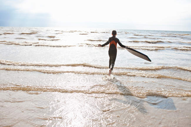 Дівчина в гідрокостюмі біжить на хвилі — стокове фото